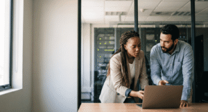 Network administrator and colleague reviewing a remote-access migration decision on a laptop in a modern office