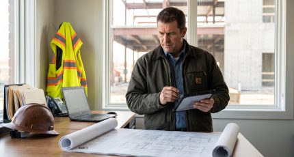 Site manager with a tablet in a well-organised construction site office, plans on the desk and daylight through the window
