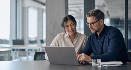 Two mid-market IT decision-makers comparing SASE options on a laptop in a modern European office
